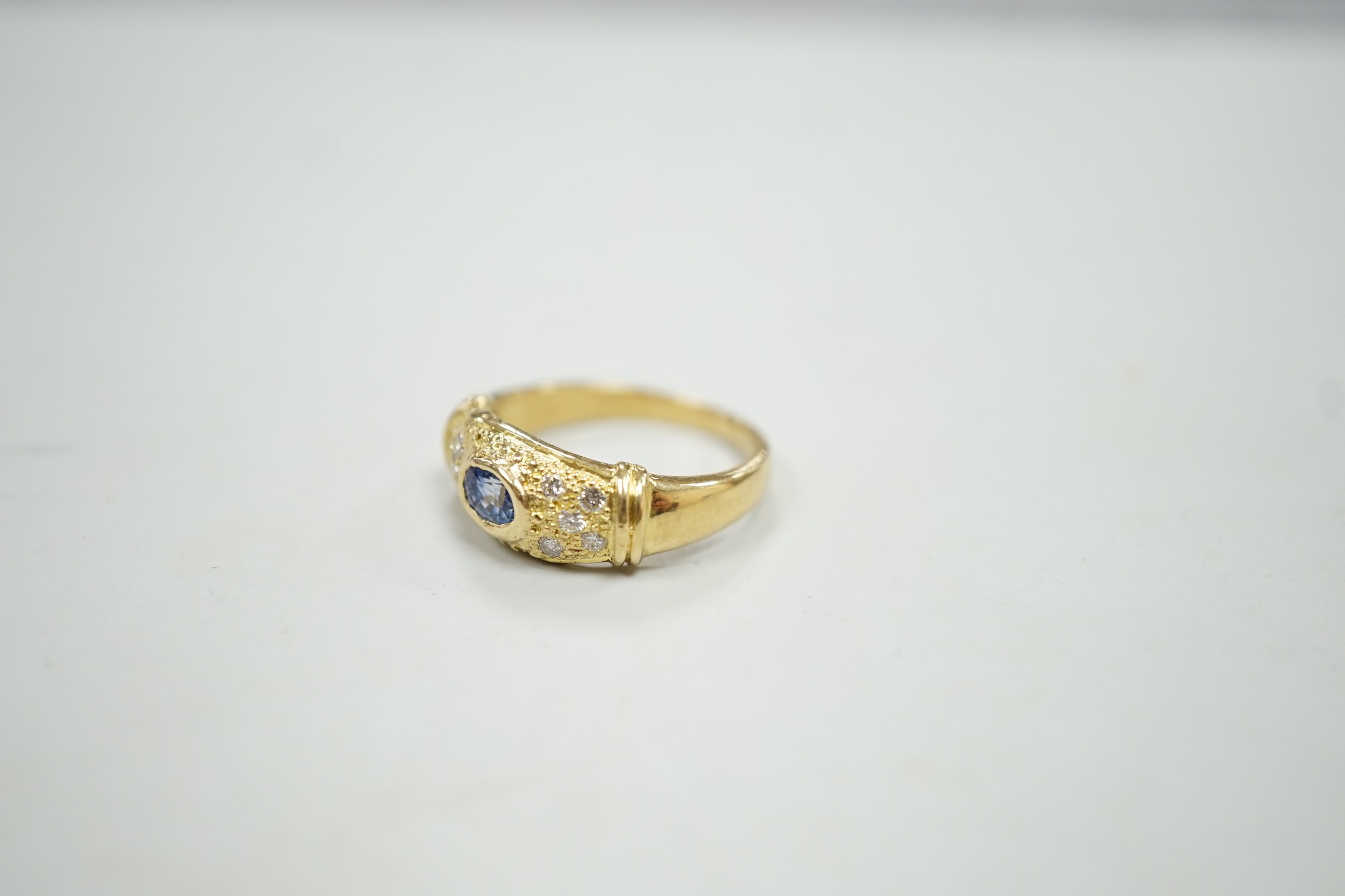 A modern 18ct gold, single stone oval cut sapphire and ten stone diamond chip set ring, size N/O, gross weight, 5.3 grams.